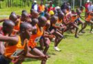 Junior runners competing in a cross country race at Kericho County, wearing colorful school athletics kits, sprinting through grassy terrain during the championships.